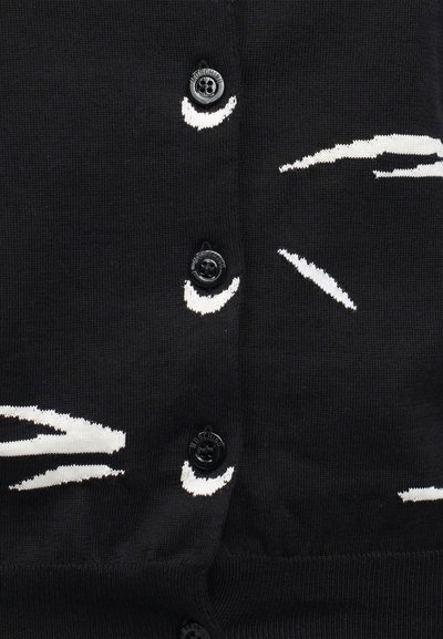 Μαύρο πλεκτό ύφασμα με μαύρα κουμπιά χαραγμένα με τη λέξη "Moschino" και διάσπαρτα λευκά αφηρημένα μοτίβα από πινελιές.