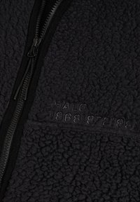 Schwarzer Sherpa-Fleece-Stoff mit geprägt-text "HALO 196819721981" und einem schwarzen Reißverschluss mit zwei Schiebern.