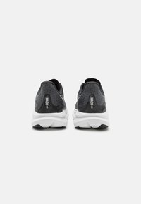 Chaussures de sport noires et grises avec une tige en mesh texturé, une semelle intermédiaire blanche rembourrée et une semelle en caoutchouc. Présente une marque au niveau du talon.