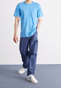 Světle modré bavlněné tričko s kulatým výstřihem a kapsou na prsou, v kombinaci s tmavě modrými cargo kalhotami. Bílé tenisky s modrými akcenty.