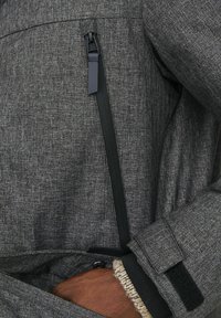 Grå tekstureret jakke med en sort lynlås, fleeceforede manchetter og en sidelomme. Stoffet har et let meleret mønster.