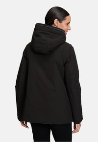 Veste à capuche noire avec une finition mate, conçue avec une coupe décontractée, une capuche surdimensionnée et des détails de couture visibles au niveau du col.