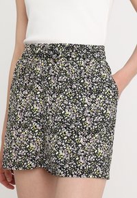 Shorts neri con motivo floreale, realizzati in un tessuto stampato con fiori rosa e gialli, cintura elastica e tasche laterali.