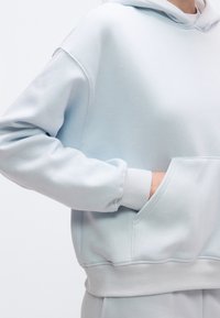 Camisola com capuz azul claro em tecido macio, bolso canguru e punhos e barra canelados. O design apresenta um ajuste descontraído e textura suave.