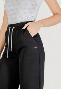 Pantalones jogger negros con tejido texturizado, cintura elástica y cordón. Presenta bolsillos laterales y un discreto detalle de logo en la pierna.