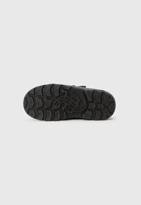 Suela de zapato de goma negra con una superficie texturada y estampada, que presenta una impresión de logo y surcos profundos para tracción.