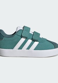 Tyrkysové semišové tenisky s bílými pruhy, vybavené suchými zipy, kulatou špičkou a bílou gumovou podrážkou pro lepší přilnavost a odolnost.