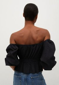 Schwarzes, schulterfreies Oberteil mit puffärmeln, strukturiertem Stoff, tailliertem Schnitt und peplum Saum, kombiniert mit Denim-Jeans.