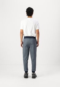 Blaue gemusterte Jogginghosen mit schmalem Schnitt, ausgestattet mit einem gerippten Bund und seitlichen Streifen, kombiniert mit einem weißen T-Shirt und schwarzen Sneakers.