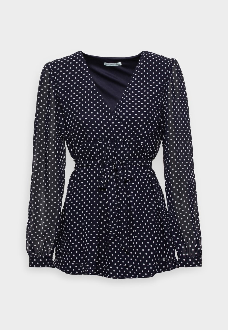 Tmavě modrá halenka s puntíky, průhledné dlouhé rukávy, výstřih do V, zvýrazněný pas s ozdobnou mašlí a texturovaná látka s bílými puntíky po celém povrchu.