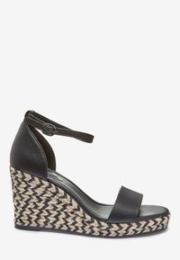 Sandalia de cuña de cuero negro con un tacón de yute trenzado en beige y negro. Presenta una amplia tira frontal y una correa de tobillo ajustable con hebilla de metal.
