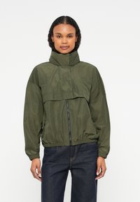 Ελαφρύ μπουφάν ελιάς με ψηλό γιακά, φερμουάρ μπροστά και ελαστική μέση. Διαθέτει άνετη εφαρμογή και μακριά μανίκια.