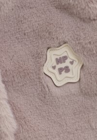 Miękka, bladoróżowa tkanina z włókna sztucznego, z białą łatą w kształcie gwiazdy, na której znajduje się lawendowy napis "NP PS" oraz drobne akcenty w kształcie serca.