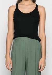 Svart ribbad linne med smala axelband, figurnära design, mjuk textur. Kombinerat med olivgröna, högmidjade, veckade byxor.