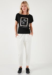 Zwarte korte mouwen t-shirt met bloemenprint en gouden lijstdetails, gecombineerd met aangesloten witte broeken en zwarte sneakers. Zachte katoenmix stof.