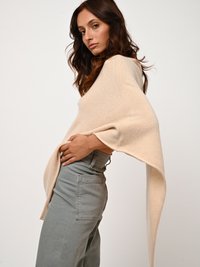 Beige Oversized-Pullover mit weiten Ärmeln und verlängertem Rücken. Ein Paar hellgraue High-Waist-Jeans mit sichtbarem Gesäßtaschendetail.