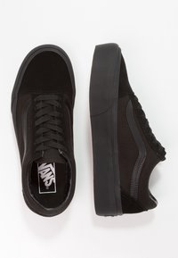 Baskets Vans noires avec lacets, une chaussure vue de dessus et l'autre de côté, montrant le logo à l'intérieur.