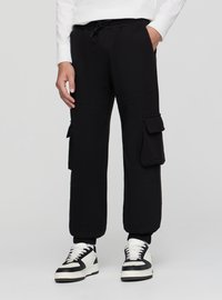 Czarne spodnie dresowe z elastycznym pasem i sznurkiem do regulacji, z dwoma bocznymi kieszeniami typu cargo i ściągaczami na końcach nogawek. Do tego czarno-białe sneakersy.