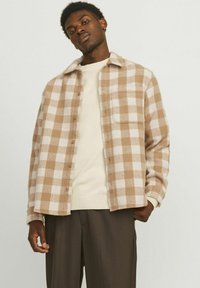 Brown and cream check-patterned flannel shirt with a button-down front, collar, and single chest pocket, worn over a cream sweater.