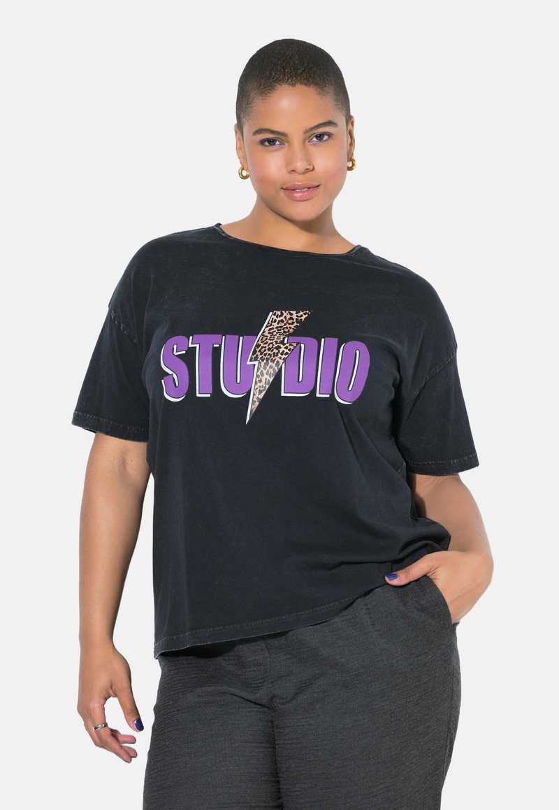 Černé oversized tričko s leopardím potiskem blesku a výrazným fialovým nápisem "STUDIO." Měkká bavlněná tkanina s krátkými rukávy.