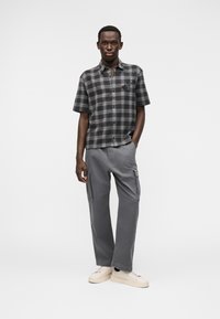 Πουκάμισο με κοντά μανίκια σε γκρι και μαύρο καρό, σε συνδυασμό με γκρι παντελόνι cargo. Παπούτσια είναι αθλητικά σε κρεμ απόχρωση.