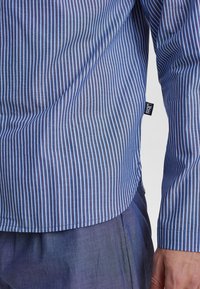 Blauw-wit gestreepte shirt met lange mouwen, van katoen, met een gebogen zoom en een klein merketiket aan de zijkant. Gladde textuur.