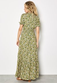 Vestido largo verde con flores, mangas cortas abullonadas, cintura elástica y falda fluida. Presenta un pequeño patrón de margaritas en amarillo y blanco.