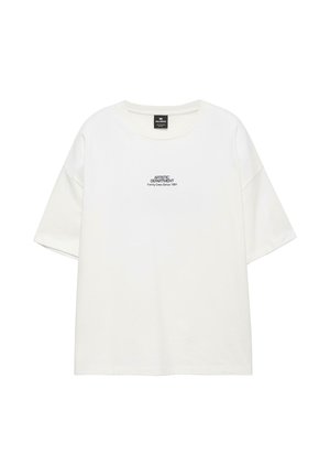 Jeune homme aux cheveux courts et bouclés portant un t-shirt blanc à col rond avec l'inscription « ARTISTIC DEPARTMENT Family Crew Since 1991 » sur la poitrine.
