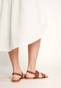 Braune Ledersandale mit einem Leopardenmuster-Panel, flacher Sohle, Knöchelriemen mit Schnallendetail und minimalistischem Design.