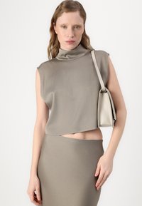 Hellgraues, ärmelloses Oberteil mit hohem Kragen und verkürztem Design, kombiniert mit einem passenden Rock. Eine kleine cremefarbene Handtasche hängt an der Schulter.