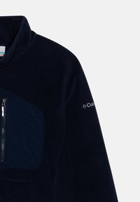 Pull à col montant en polaire marine avec poche poitrine zippée et texture douce. Comprend le logo Columbia sur la manche.