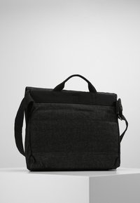 Bolsa mensajera negra de tela con forma rectangular, asas en la parte superior, correa de hombro ajustable y un acabado mate texturizado.