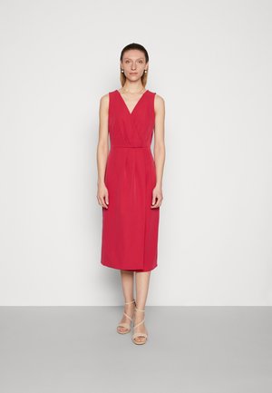 Vestido midi justo sem mangas em rosa vibrante, com decote em V e pregas subtis. Combinado com sandálias bege de tiras.