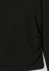 Haut noir à manches longues en coton doux, présentant un design simple avec un léger froncage sur le côté et un ourlet arrondi.