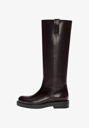 Knee-high brązowe skórzane kozaki o gładkiej fakturze, okrągłym nosie i płaskiej czarnej gumowej podeszwie. Posiadają pionową szew i tylną pętlę.