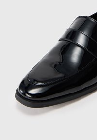 Schwarzer Lackleder-Loafer mit einer glatten, glänzenden Oberfläche. Eigenschaften sind eine leicht zugespitzte Zehenform und ein minimalistischer Riemenakzent am Vorderfuß.