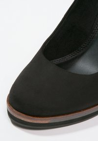 Chaussure à talon haut en daim noir avec bout rond, texture lisse et un accent en bois brun sur la semelle pour un contraste.