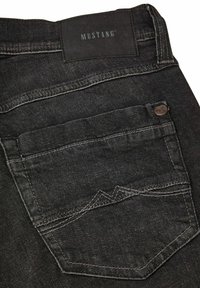 Jeans de mezclilla negra con un distintivo bolsillo trasero con detalles de costura, una etiqueta de cuero de marca y una textura suave.