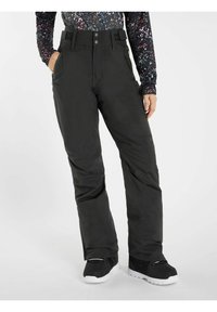 Osoba ubrana w czarne ocieplane spodnie narciarskie z zamykanymi na zamek bocznymi kieszeniami oraz czarne buty zimowe na tle jednolitego białego tła.