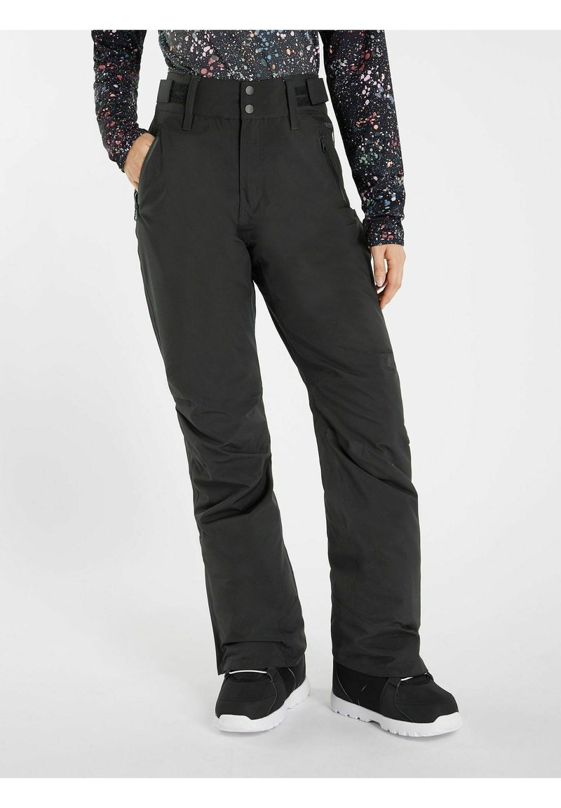 Osoba ubrana w czarne ocieplane spodnie narciarskie z zamykanymi na zamek bocznymi kieszeniami oraz czarne buty zimowe na tle jednolitego białego tła.