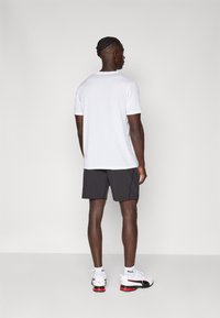 Hvit t-skjorte med korte ermer parret med mørkegrå shorts. T-skjorten har rund hals; antrekket inkluderer hvite sportsko med røde detaljer.