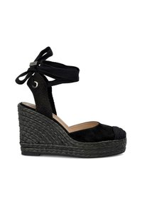 Sandale compensée en daim noir avec un talon en jute tressé, un bout rond et des liens à la cheville. Présente une bride en tissu noir texturé au niveau du talon.