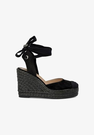 Schwarze Wildleder-Wedge-Sandale mit geflochtenem Jute-Absatz, runder Zehenpartie und Knöchelbindern. Verfügt über ein strukturiertes schwarzes Stoffband am Absatz.