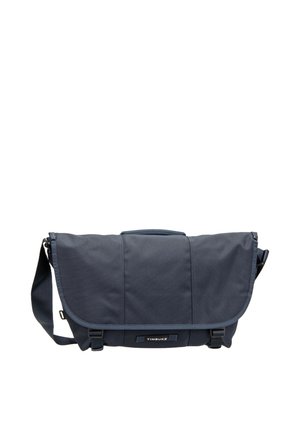 Dunkelblaue Timbuk2 Messenger-Tasche mit verstellbarem Schultergurt, Frontklappe und zwei schwarzen Steckverschlüssen auf weißem Hintergrund.