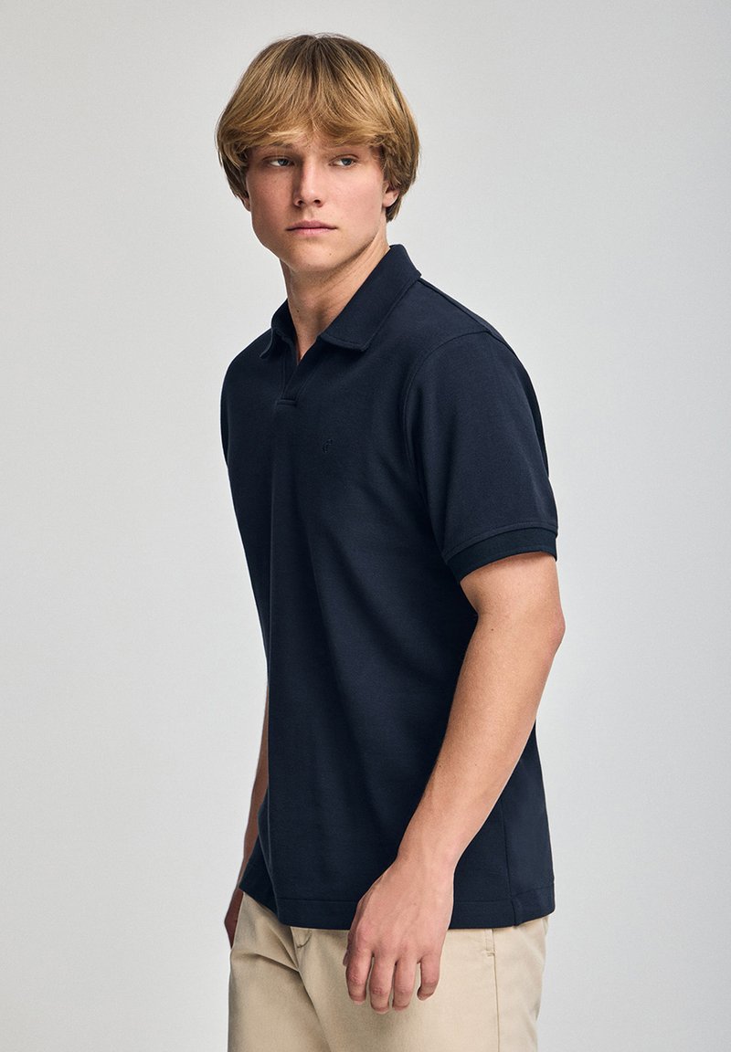 Polo shirt azul marino hecho de una tela suave, con un cuello clásico, mangas cortas y un logo discreto en el lado izquierdo del pecho.