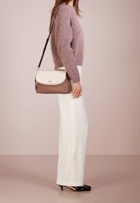 Soft pink wool sweater, white tailored pants with side slits, and a two-tone satchel bag in cream and taupe. Pointed black heels visible.