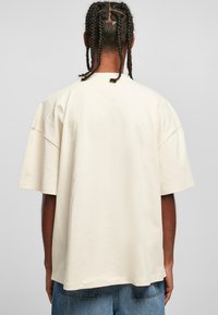 Béžové oversized tričko s kulatým výstřihem a krátkými rukávy, vyrobené z měkké bavlny, s čistým, minimalistickým designem a rovným lemem.