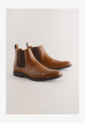 Bottes Chelsea en cuir marron avec panneaux latéraux élastiques, texture lisse, bout arrondi et talon bas empilé. Détails de couture subtils.