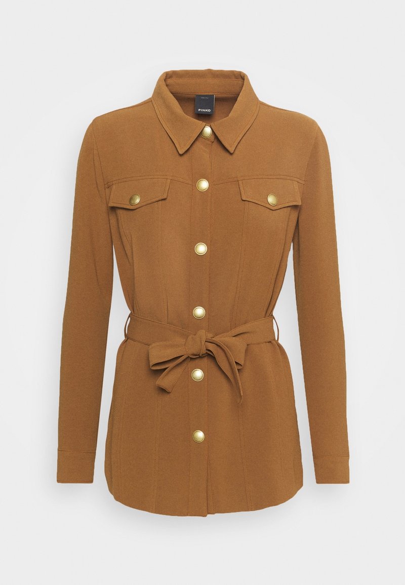 Giacca marrone su misura in un tessuto morbido, con chiusura a bottoni, due tasche sul petto e un dettaglio in vita annodato con bottoni color oro.