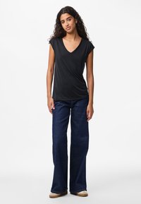 Juodas trumpomis rankovėmis V formos iškirptės viršus su apsiaustu, derinamas su plačiomis tamsiai mėlyno džinso plačiomis kojomis kelnėmis ir šviesios spalvos plokščiais batais.